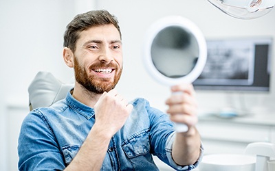 Male dental patient sitting and smiling at handheld mirror