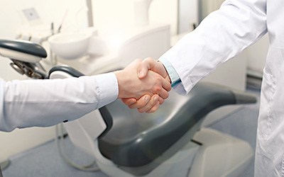 Close-up of dentist and patient shaking hands in front of treatment chair