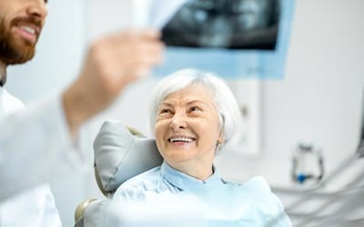 An older woman smiling at her dentist as he shows her a dental X-Ray of her smile