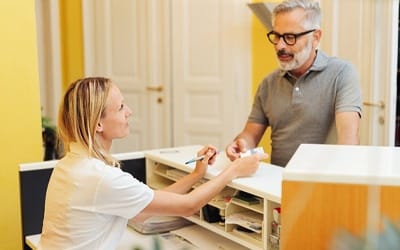 A male patient handing information to a dental receptionist