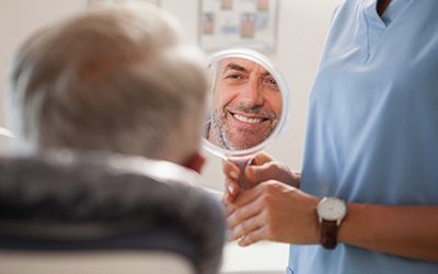 Dentist holding up mirror so patient can examine smile
